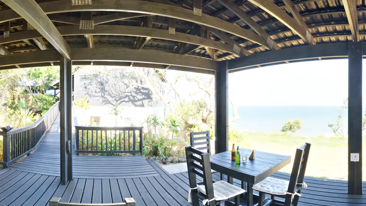 Überdachte Restaurant-Terrasse mit Holztischen und Blick aufs Meer